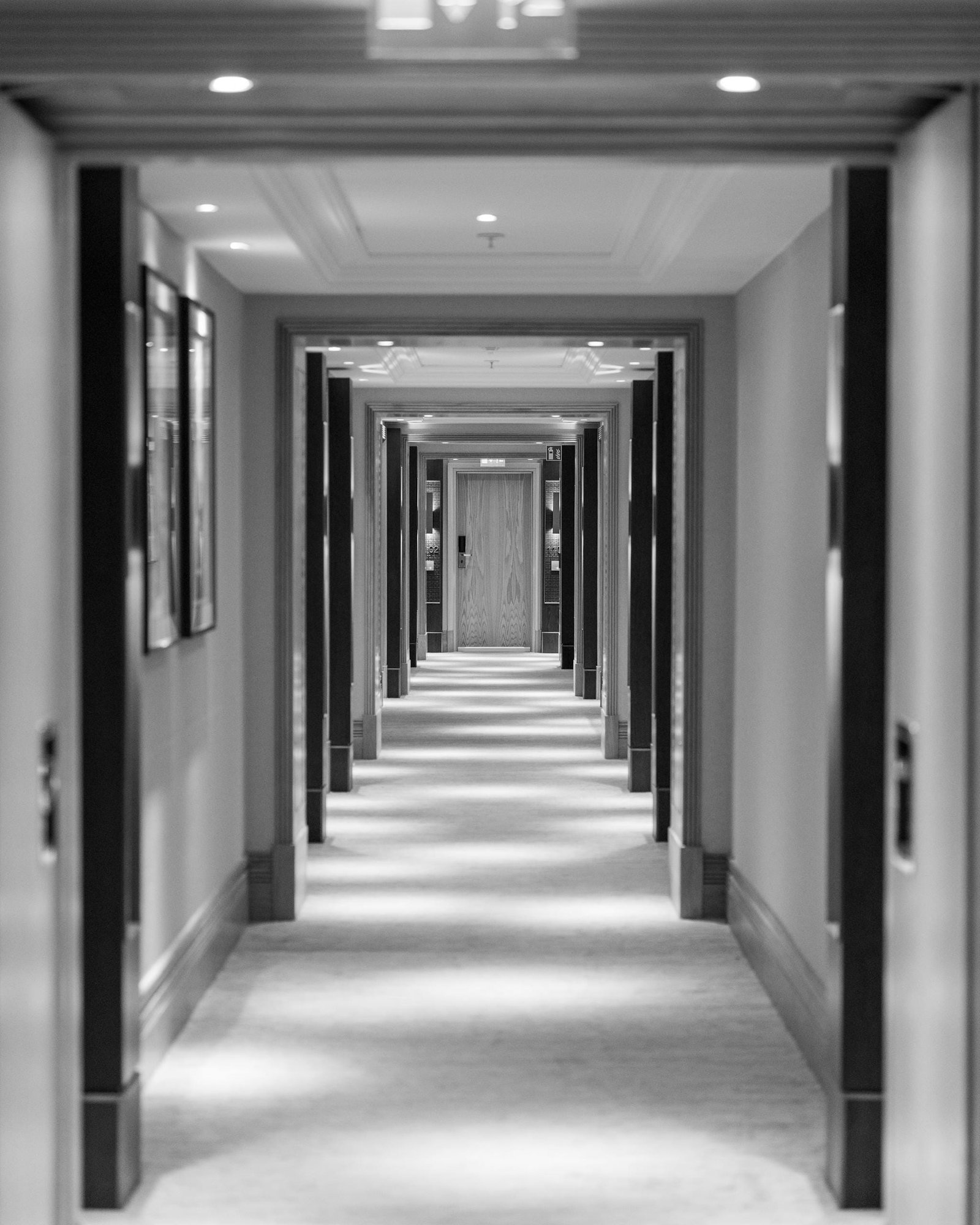 A symmetrical black and white view of a hotel corridor with illuminated lighting and doorways.